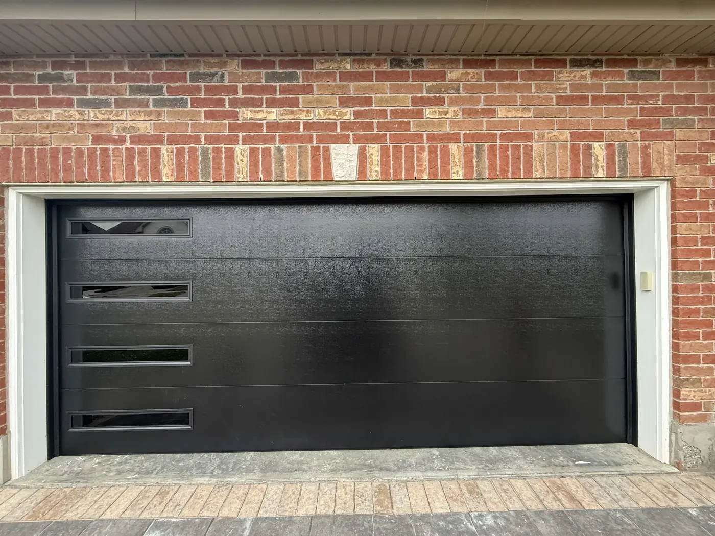 Black modern garage door with side windows on a brick home