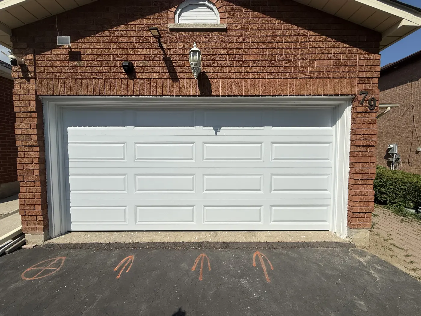 White raised panel garage door on a brick home, a replacement door style our team installs in Toronto